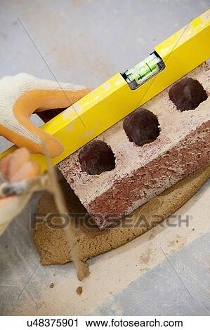 Stock Image - Close up of bricklayers hands using spirit level on brick. Fotosearch