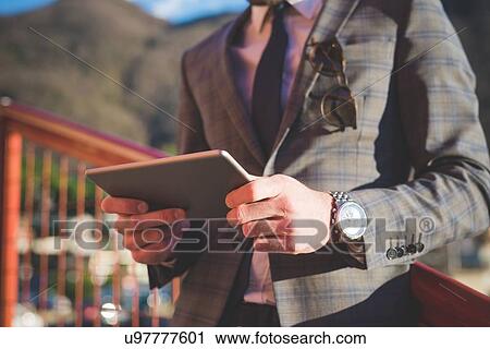 Stock Image - Cropped close up of young man using digital tablet on footbridge. Fotosearch