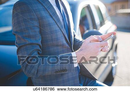Cropped shot of young businessman leaning against car using smartphone View Large Photo Image Stock Photograph - Cropped shot of young businessman leaning against car using smartphone. Fotosearch