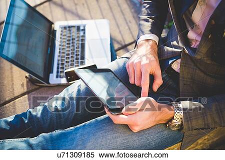 Stock Photography - Cropped shot of young mans using digital tablet and laptop on sidewalk. Fotosearch