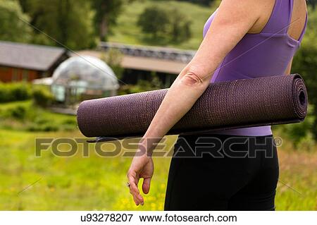 Stock Photo - Cropped view of mature woman carrying yoga mat in eco lodge field. Fotosearch