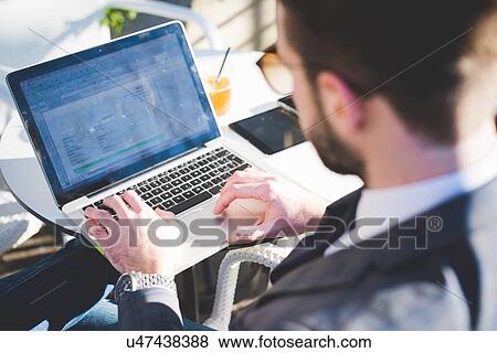 Stock Photo - Cropped view of young businessman using laptop at sidewalk cafe. Fotosearch