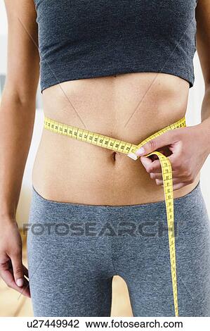 Cropped view of young woman measuring her waist with tape measure View Large Photo Image Stock Image - Cropped view of young woman measuring her waist with tape measure. Fotosearch