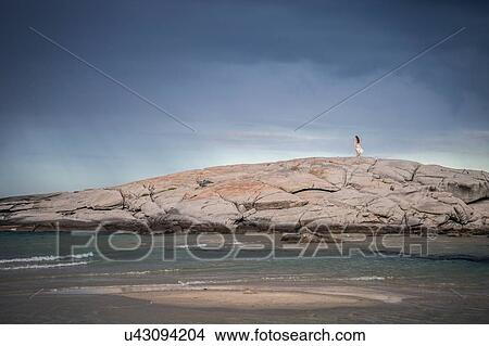 Picture - Distant view of young woman strolling on rock formation at coast, Costa Rei, Sardinia, Italy. Fotosearch