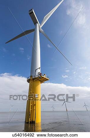Stock Image - Engineer climbing wind turbine from boat at offshore windfarm. Fotosearch