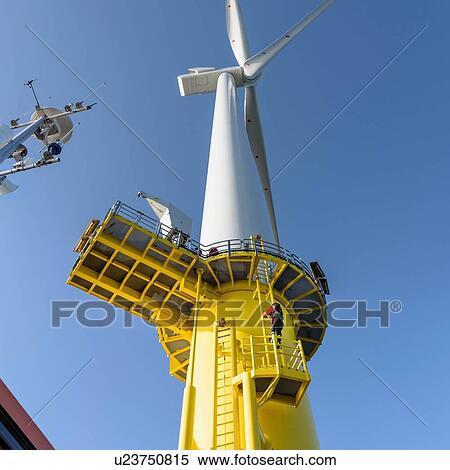 Stock Photography - Engineer climbing wind turbine from boat at offshore windfarm, low angle view. Fotosearch