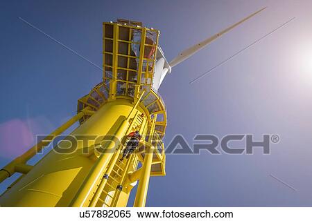 Stock Photography - Engineer climbing wind turbine from boat at offshore windfarm, low angle view. Fotosearch