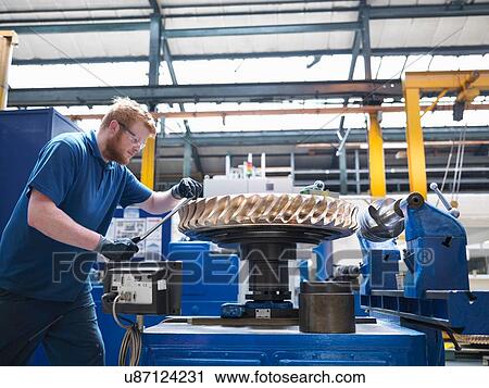 Stock Image - Engineer finishing bronze gear wheel in engineering factory. Fotosearch