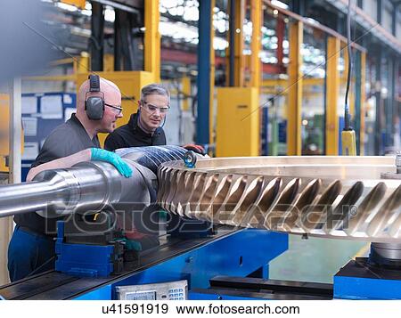 Stock Photo - Engineer inspecting worm gears in engineering factory. Fotosearch
