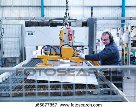 Stock Photo - Engineer loading sheet metal into laser cutter in engineering factory. Fotosearch