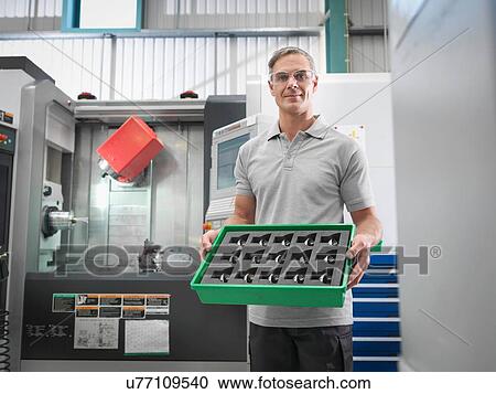 Stock Image - Engineer with CNC lathe holding machined products in orthopaedic factory, portrait. Fotosearch