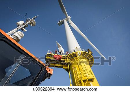 Picture - Engineers climbing wind turbine from boat at offshore windfarm, low angle view. Fotosearch