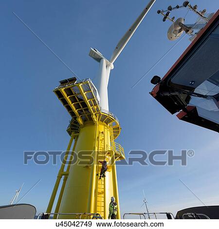 Stock Photo - Engineers climbing wind turbine from boat at offshore windfarm. Fotosearch
