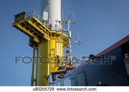 Stock Photo - Engineers climbing wind turbine from boat at offshore windfarm. Fotosearch