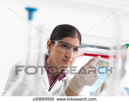 Stock Photography - Female biologist in laboratory, holding a flask containing stem cells. Fotosearch
