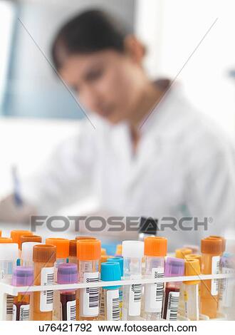 Stock Image - Female doctor making notes on blood and urine samples at desk. Fotosearch
