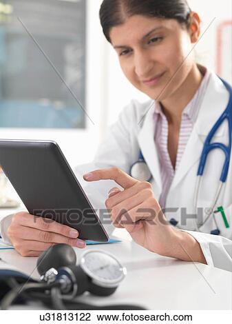 Stock Image - Female doctor updating medical records using digital tablet. Fotosearch