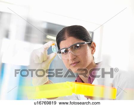 Female scientist holding up and examining chemical sample in lab View Large Photo Image Stock Photo - Female scientist holding up and examining chemical sample in lab. Fotosearch