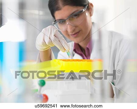 Stock Image - Female scientist looking at chemical sample in lab. Fotosearch