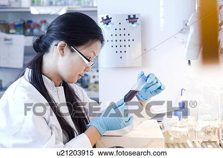 Stock Photography - Female scientist looking at specimen bottle in laboratory. Fotosearch
