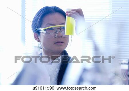 Stock Photograph - Female scientist looking at yellow specimen in laboratory. Fotosearch