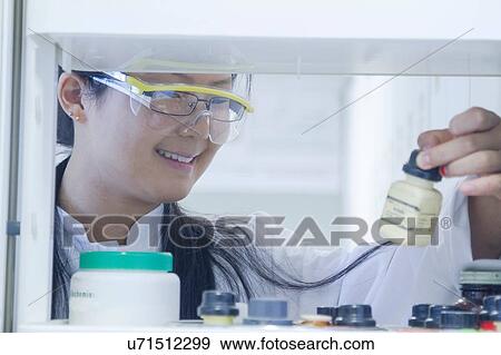 Stock Photo - Female scientist selecting chemical from shelf in laboratory. Fotosearch