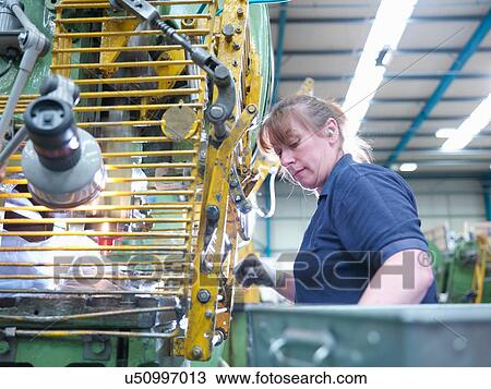 Stock Image - Female worker operating punch machine in engineering factory. Fotosearch