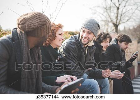 Five young adult friends using smartphones and digital tablets in park View Large Photo Image Picture - Five young adult friends using smartphones and digital tablets in park. Fotosearch