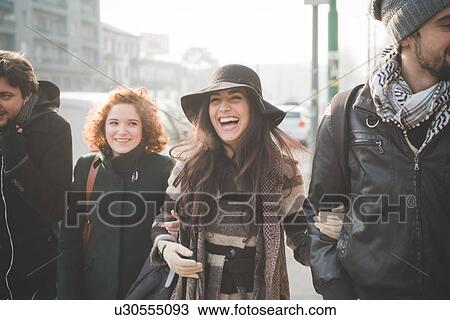 Stock Image - Four young adult friends strolling arm in arm along city street. Fotosearch