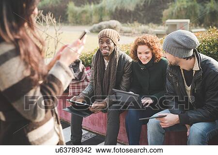 Four young adult friends using smartphones and digital tablets in park View Large Photo Image Stock Image - Four young adult friends using smartphones and digital tablets in park. Fotosearch