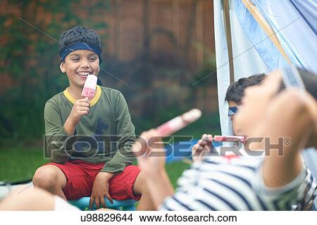 Girl and two brothers eating ice lollies in garden View Large Photo Image Picture - Girl and two brothers eating ice lollies in garden. Fotosearch