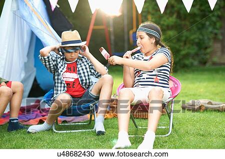 Girl and two brothers eating ice lollies in front of homemade tent in garden View Large Photo Image Stock Image - Girl and two brothers eating ice lollies in front of homemade tent in garden. Fotosearch
