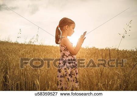 Stock Photo - Girl concentrating on smartphone touchscreen in wheat field. Fotosearch