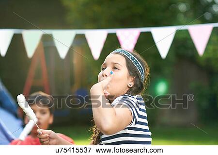 Stock Photo - Girl eating toasted marshmallows in garden. Fotosearch
