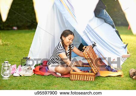 Stock Image - Girl emptying picnic basket in front of homemade tent in garden. Fotosearch