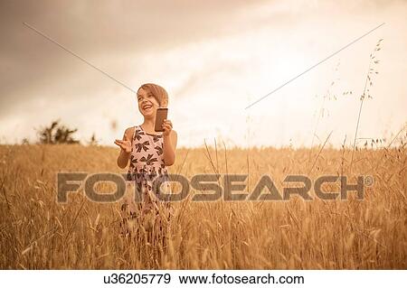 Stock Photo - Girl using smartphone whilst laughing in wheat field. Fotosearch
