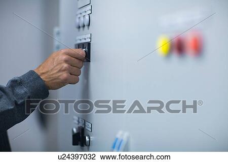 Stock Image - Hand of male technician pressing switch on control panel. Fotosearch