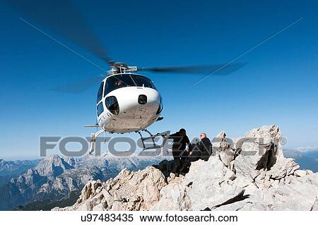 Stock Photography - Helicopter dropping BASE jumpers on mountain, Dolomites, Italy. Fotosearch