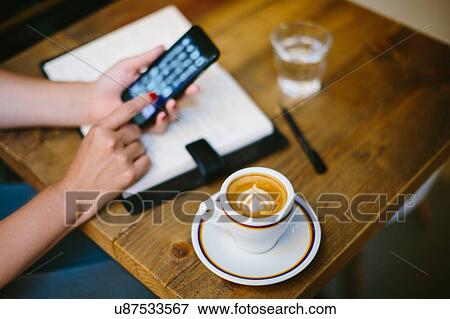 High angle view of coffee cup on table and womans hands using smartphone View Large Photo Image Stock Photo - High angle view of coffee cup on table and womans hands using smartphone. Fotosearch