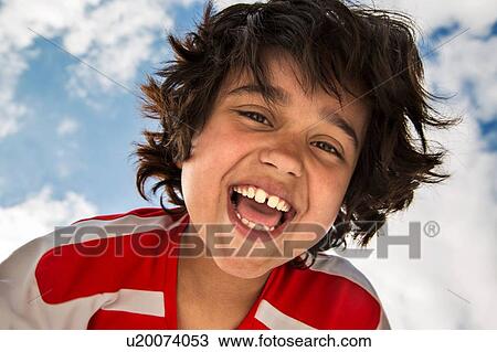 Stock Image - Low angle portrait of smiling boy in front of sky. Fotosearch