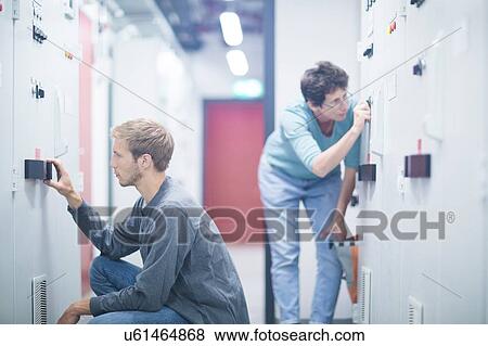Stock Photo - Male and female technicians turning switches in technical room. Fotosearch
