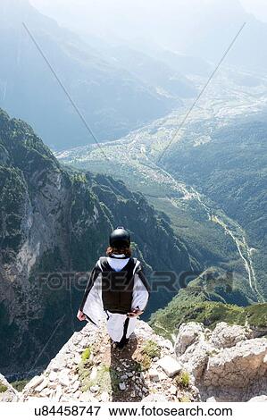 Stock Photo - Male BASE jumper in wingsuit standing on edge of mountain, Dolomites, Italy. Fotosearch