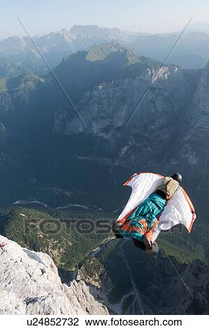 Stock Image - Male BASE jumper wingsuit flying from mountain, Dolomites, Italy. Fotosearch