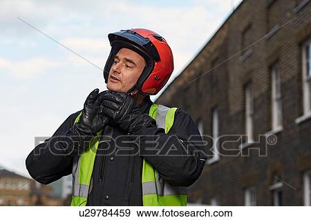 Stock Photo - Male motor scooter rider fastening crash helmet in street. Fotosearch