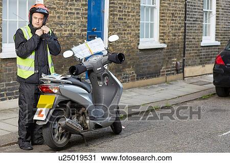 Stock Image - Male motor scooter rider in street fastening crash helmet. Fotosearch