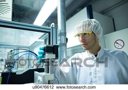 Stock Image - Male scientist looking at equipment in lab cleanroom. Fotosearch