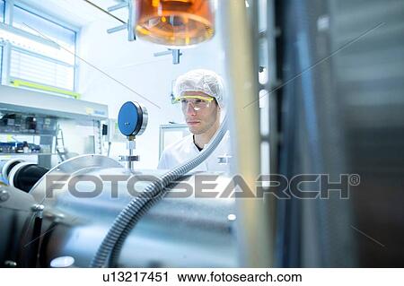 Stock Image - Male scientist reading equipment gauge in lab cleanroom. Fotosearch