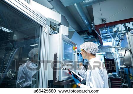 Stock Image - Male scientist with notebook adjusting control panel in lab cleanroom. Fotosearch