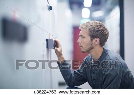 Stock Image - Male technician crouching to turn switch in technical room. Fotosearch