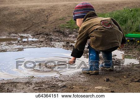 Male toddler wearing rubber boots playing with stick in puddle View Large Photo Image Stock Image - Male toddler wearing rubber boots playing with stick in puddle. Fotosearch